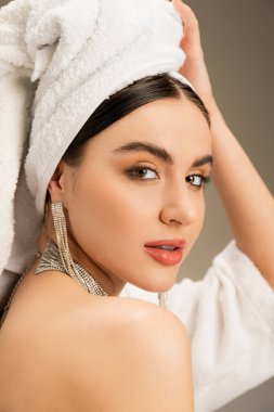 brunette woman with makeup touching white towel on head on grey background 