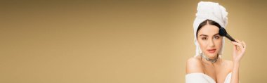 charming woman with white towel on head applying face powder with makeup brush on beige background, banner 
