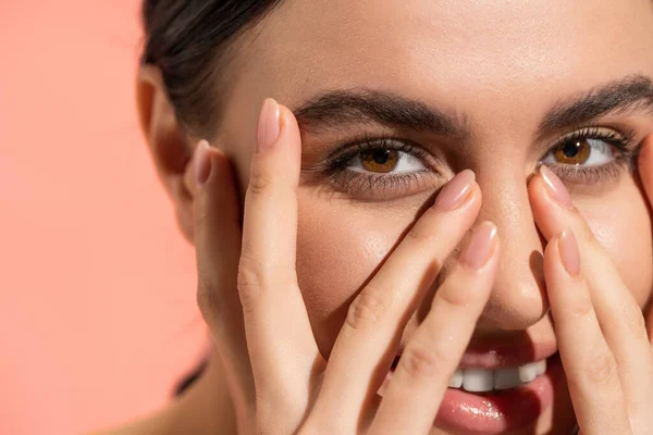 stock image close up view of happy young woman covering face while looking at camera isolated on pink 