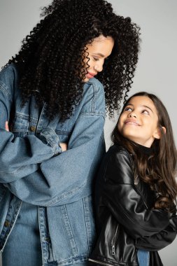 Smiling mom and child crossing arms while looking at each other isolated on grey 