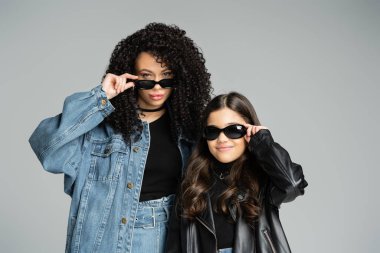 Trendy mother and daughter in sunglasses posing isolated on grey 
