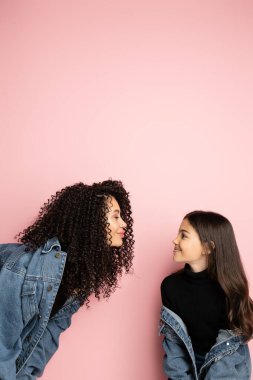 Pembe arka planda duran kot ceketli moda anne ve çocuğun yan görüntüsü 