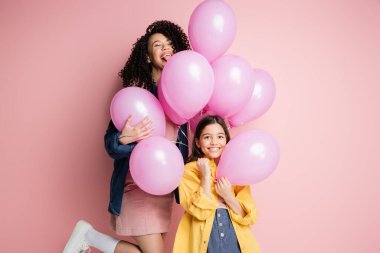 Pembe arka planda balonların yanında duran pozitif kadın ve çocuk. 