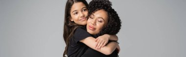 Preteen kid in t-shirt hugging curly mom isolated on grey, banner 