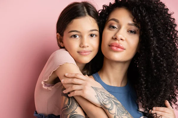 stock image Portrait of child hugging stylish mother and looking at camera on pink background 