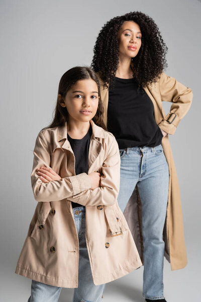 Trendy preteen kid crossing arms near blurred mom on grey background 
