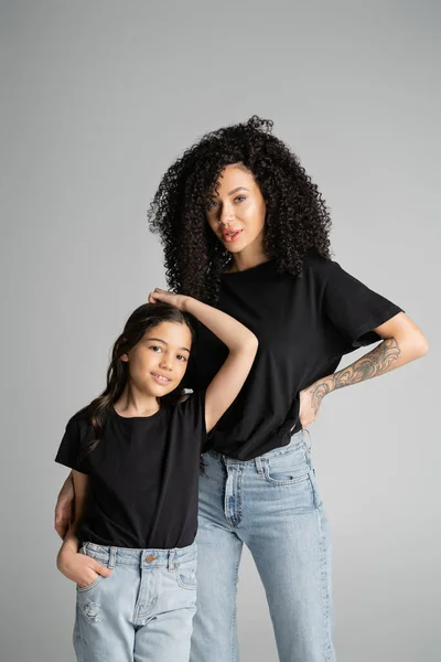 Stylish mother and daughter in black t-shirts posing isolated on grey