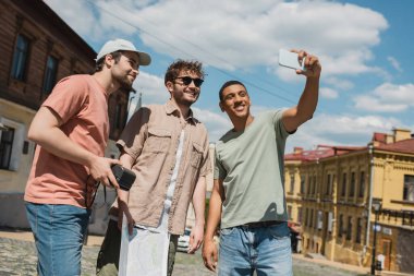 Neşeli Afrikalı Amerikalı gezgin akıllı telefondan Andrews 'da çok ırklı adamlarla fotoğraf çekiyor.