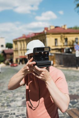 young man in sun cap taking photo on vintage camera on Andrews descent in Kyiv clipart