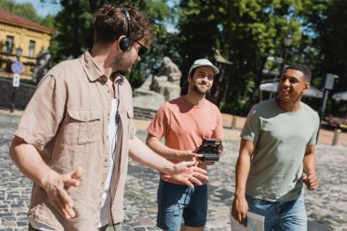 Kyiv 'e inen Andrews' de harita ve klasik kamerayla yürüyen çok ırklı turistlerin yakınında el kol gezen kulaklıklı tur rehberi