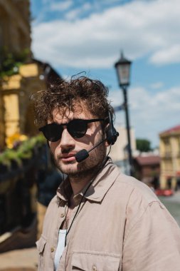 Güneş gözlüklü ve kulaklıklı genç tur rehberinin portresi Kyiv 'deki bulanık Andrews' da kameraya bakıyor.