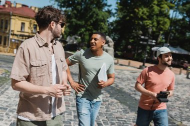 happy african american tourist with travel map talking to guide during walk on Andrews descent in Kyiv clipart