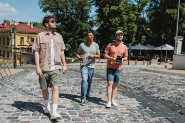 Kyiv 'de Andrews kaldırımında yürüyen haritalı ve klasik kameralı tam uzunlukta tur rehberi ve çok kültürlü gezginler.