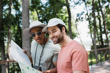 Bulanık parktaki seyahat haritasına bakan güneş şapkalı pozitif çoklu etnik turistler