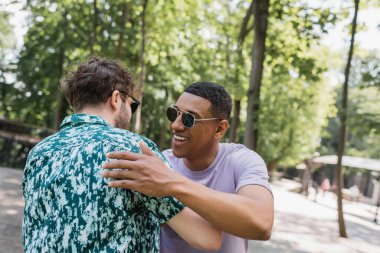 Pozitif Afro-Amerikalı adam yaz parkında güneş gözlüklü arkadaşına sarılıyor. 