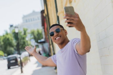 Güneş gözlüklü neşeli Afro-Amerikalı adam Kyiv 'de akıllı telefondan video görüşmesi yapıyor. 