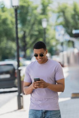 Yazın şehir caddesinde güneş gözlüklü Afro-Amerikan adam akıllı telefon kullanıyor. 