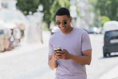 Kaygısız Afro-Amerikalı güneş gözlüklü adam şehir caddesinde cep telefonu kullanıyor. 