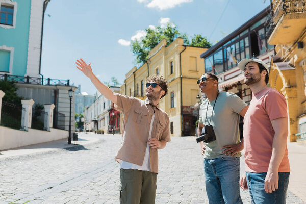 tour guide in sunglasses pointing with hand during excursion with interracial tourists on Andrews descent in Kyiv