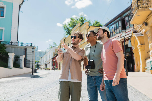 Улыбающийся гид с пальцем на мобильный телефон во время экскурсии для межрасовых мужчин по Подольскому району Киева
