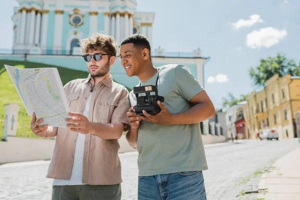 Genç tur rehberi, mutlu Afrika kökenli Amerikalı turistin yakınındaki şehir haritasına bakıyor. Andrews 'un Kyiv' e inişini gösteren eski model bir kamerayla. 