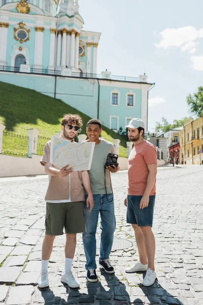 stock image young tour guide looking at city map near carefree interracial tourists on Andrews descent in Kyiv