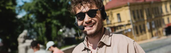 在基辅 无忧无虑的导游头戴太阳镜 头戴耳机 对着相机微笑 俯瞰着模糊的安德鲁下降的肖像 — 图库照片