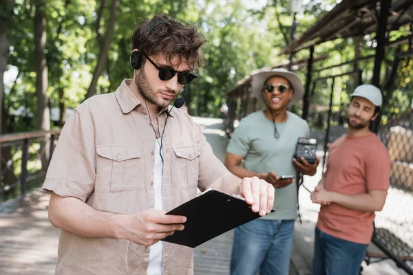 Young Guide Headset Sunglasses Holding Clipboard Route Multiethnic Travelers Blurred — Stock Photo, Image