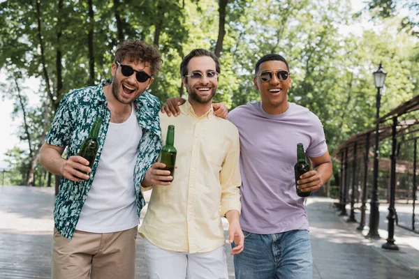 街の公園で新鮮なビールと一緒に歩くサングラスと流行の夏の衣装で楽しい多民族の友人 — ストック写真