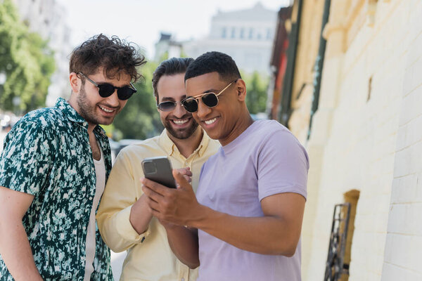 Мультиэтнические мужчины в солнечных очках с помощью смартфона на городской улице в Киеве 