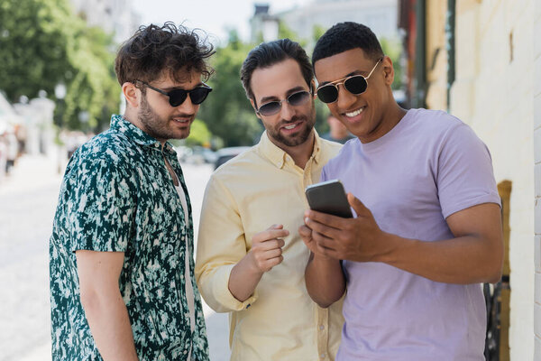 Мультиэтнические друзья используют мобильный телефон на городской улице летом 