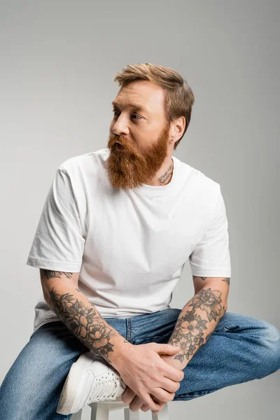 Getatoeëerde Man Jeans Shirt Zittend Stoel Geïsoleerd Grijs — Stockfoto