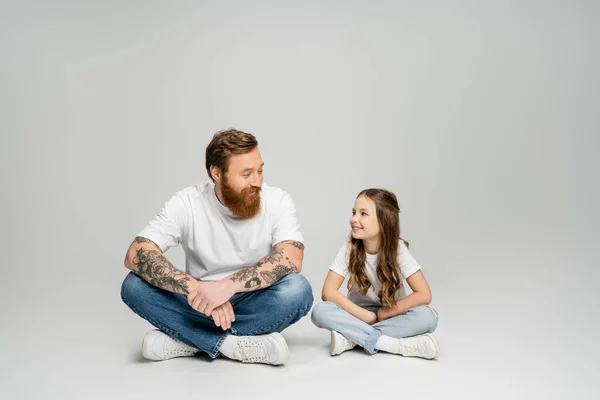 Glimlachend Meisje Praten Met Getatoeëerde Vader Terwijl Zitten Grijze Achtergrond — Stockfoto