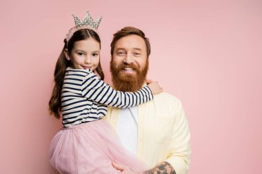 Pozitif ve dövmeli bir baba pembe bantlı kızını tutuyor.  