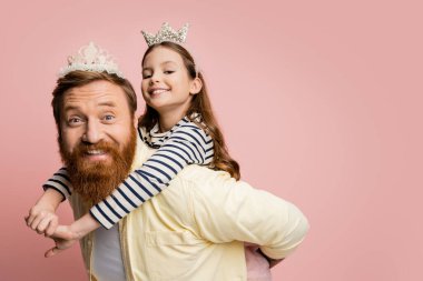Neşeli çocuk babasından faydalanıyor. Taçlı saç bandı pembe renkte.  