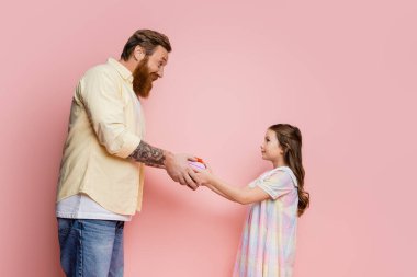 Pembe arka planda Babalar Günü 'nde dövmeli babaya hediye veren çocuk yan görünümü 