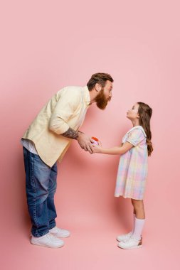 Erkeğin dudaklarını bükerken pembe arka planda kızına hediye paketi vermesi. 