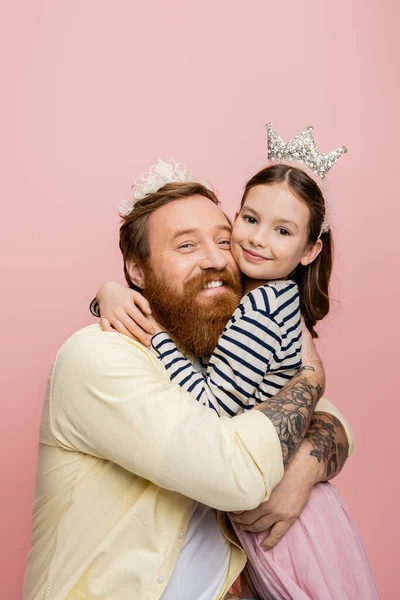 Stock image Cheerful father and daughter in crowns hugging isolated on pink  