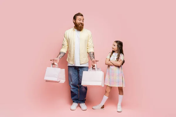 분홍색 배경에 쇼핑백을 아버지 옆에서 웃으며 팔을건너는 소녀들의 — 스톡 사진
