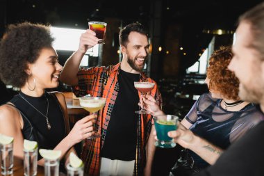 Carefree bearded man holding negroni cocktail near multiethnic friends in bar  clipart