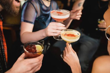 Cropped view of interracial friends holding different cocktails in bar  clipart