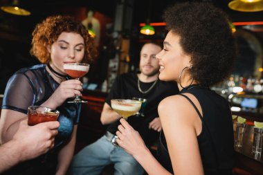 Pozitif kıvırcık Afrikalı Amerikalı kadın barda arkadaşlarının yanında Pisco kokteyli tutuyor. 