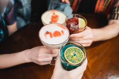 Cropped view of friends clinking with different cold cocktails in bar  clipart
