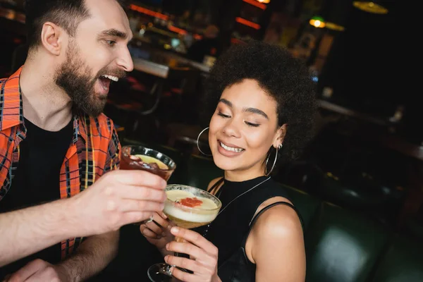 在酒吧里 一个兴奋的男人在卷曲的非洲裔美国朋友身边端着黑香肠鸡尾酒 — 图库照片