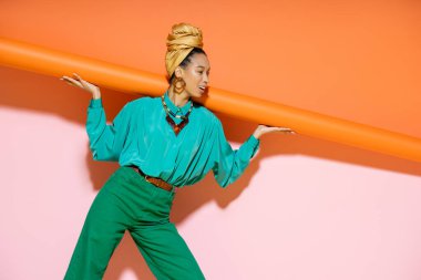 Gülümseyen Afro-Amerikan kadın moda yaz kıyafetiyle pembe ve turuncu arka planda poz veriyor. 