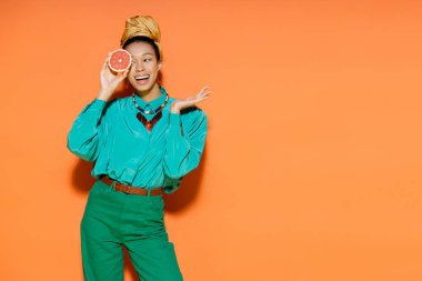 Cheerful african american model in summer clothes holding fresh grapefruit on orange background  clipart