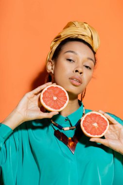 Turuncu arka planda kesik greyfurt tutan türbanlı Afro-Amerikan modelinin portresi 