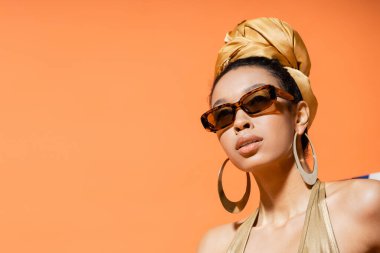 Portakala izole edilmiş türbanlı ve güneş gözlüklü Afro-Amerikan modelinin portresi. 