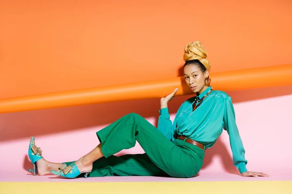 Renkli Arka Planda Oturan Türbanlı Modaya Uygun Afro Amerikan Modeli — Stok fotoğraf
