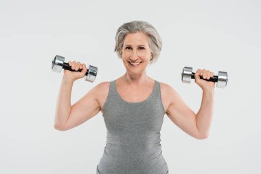 Heyecanlı, gri saçlı, gri halterli yaşlı kadın, gri renkli halterlerle egzersiz yapıyor. 